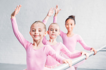 adorable multiethnic kids practicing ballet and smiling at camera in ballet studio