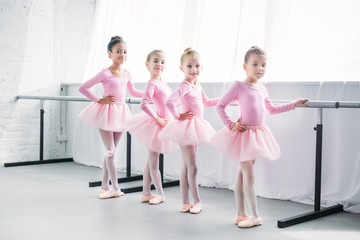 cute multiethnic kids in pink tutu skirts exercising and smiling at camera in ballet studio © LIGHTFIELD STUDIOS