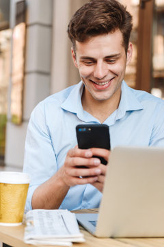 Smiling young stylish man in shirt using mobile phone up