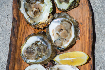 Oysters with lemon on wooden plate.