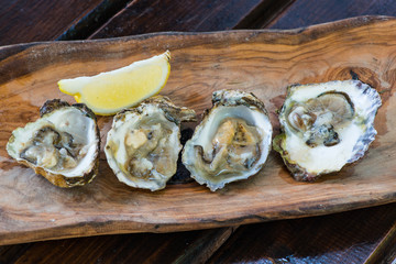 Oysters with lemon on wooden plate.