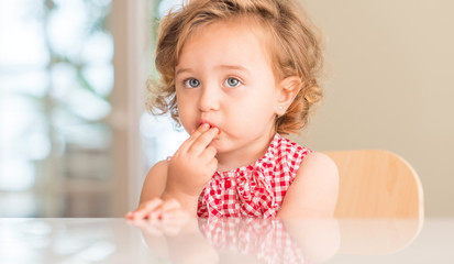 Beautiful blonde child with blue eyes eating strawberry at home.