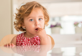 Beautiful blonde child with blue eyes eating candy and looking at the camera at home.