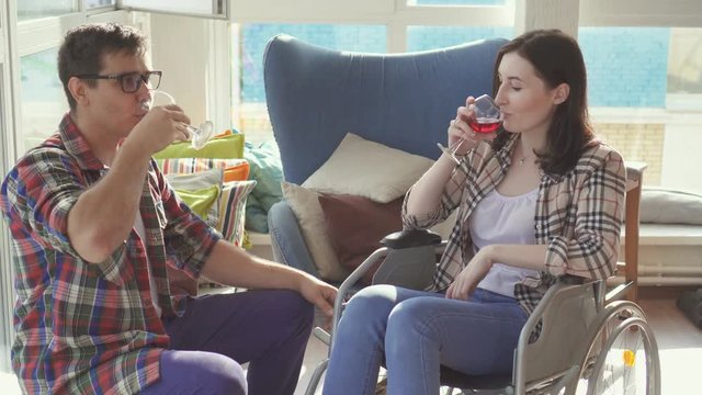 Young couple disabled girl in wheelchair and her husband drinking wine in new apartment