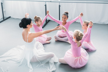 happy little ballerinas and ballet teacher sitting and holding hands in ballet school © LIGHTFIELD STUDIOS