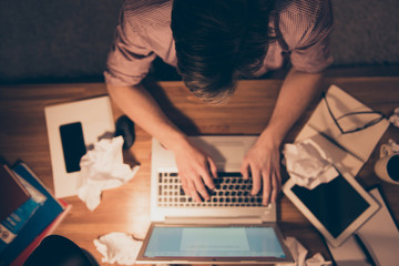 Upper angle of hard worker, attractive, busy man holding hands on keypad, having crumpled drafts on the table, taking work at home, working at night time, sitting in workplace, workstation