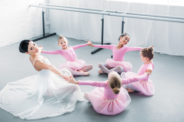 adorable little ballerinas and young teacher practicing together in ballet school
