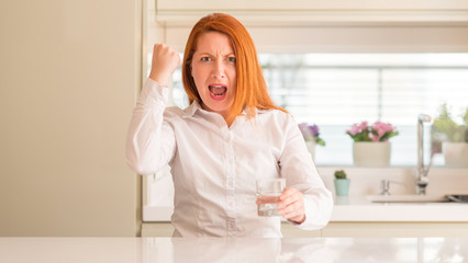 Thirsty redhead woman and glass of water annoyed and frustrated shouting with anger, crazy and yelling with raised hand, anger concept