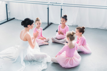 high angle view of kids in pink tutu skirts and young ballet teacher sitting together in ballet school © LIGHTFIELD STUDIOS