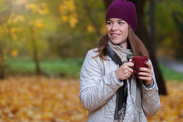 Cheerful young woman wearing coat and knitted hat enjoying fall nature in park