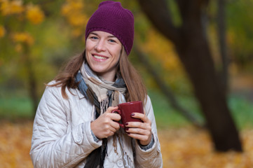 Blurred image of happy smiling young woman wearing coat and knitted hat enjoying fall nature in park