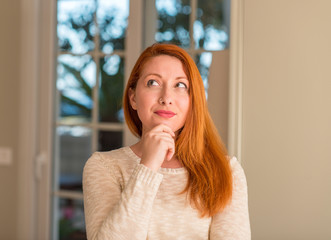 Redhead woman at home serious face thinking about question, very confused idea