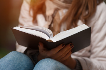 Obraz premium Close-up - Young female student with book sitting in the fall park