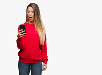 Naklejka premium Beautiful young woman using smartphone scared in shock with a surprise face, afraid and excited with fear expression