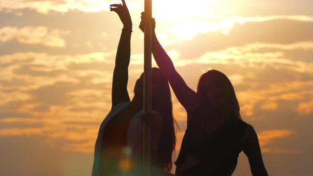 Silhouettes of two flexible women performs pole-dance at sunset