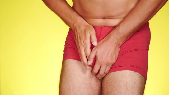 the man has problems with the genitourinary system. guy in red boxers on a yellow background. 4k, close-up, slow-motion shooting.