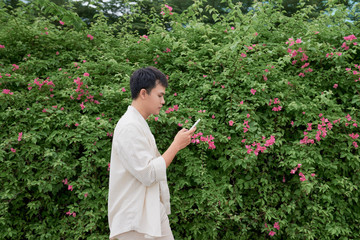 Young asian man in casual clothes on summer day and using smartphone for sending sms