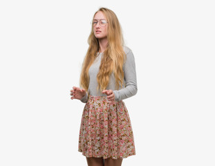Blonde teenager woman wearing flowers skirt disgusted expression, displeased and fearful doing disgust face because aversion reaction. With hands raised. Annoying concept.