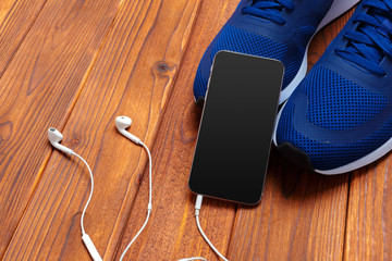Sneakers and mobile phone with headphones on wooden table