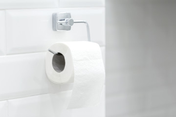 Fototapeta premium A white roll of soft toilet paper neatly hanging on a modern chrome holder