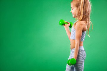 Kid girl doing fitness or yoga exercises with dumbbells isolated on green background