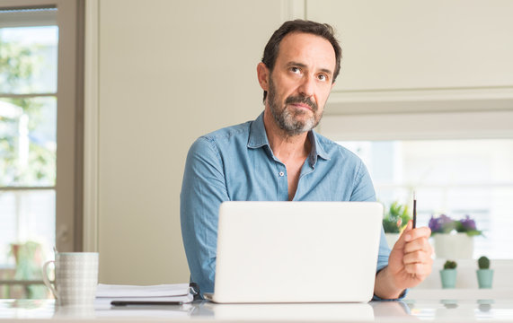 Middle age man using laptop at home with a confident expression on smart face thinking serious