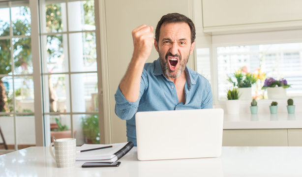 Middle age man using laptop at home annoyed and frustrated shouting with anger, crazy and yelling with raised hand, anger concept