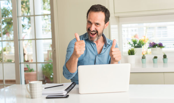 Middle age man using laptop at home happy with big smile doing ok sign, thumb up with fingers, excellent sign