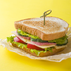 Sandwich with cheese, ham and fresh vegetables on a yellow bright background.