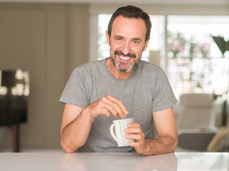 Middle age man drinking coffee in a cup with a happy face standing and smiling with a confident...