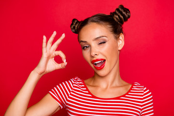 Close up portrait of happy girl with wide open mouth and wink eye gesturing ok sign isolated on vivid red background
