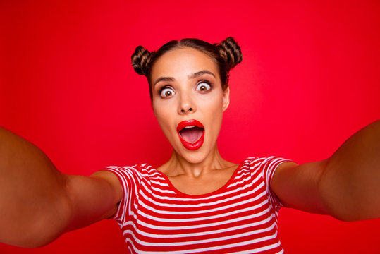 Selfie of shocked girl shooting selfie on front camera with two hands isolated on red background