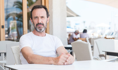 Handsome senior man sitting at terrace with a confident expression on smart face thinking serious