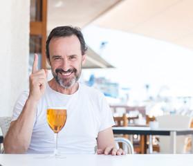 Handsome senior man drinking beer at restaurant surprised with an idea or question pointing finger with happy face, number one