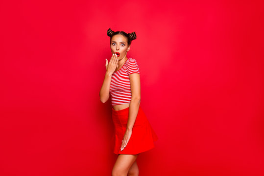 Portrait of cute and surprise girls dressed in striped tshirt and red skirt covers her open mouth with palm isolated over background