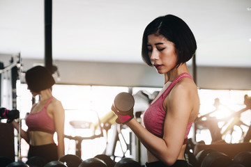 Young beautiful woman doing exercises with dumbbell in gym. Glad smiling girl is enjoying with her training process.