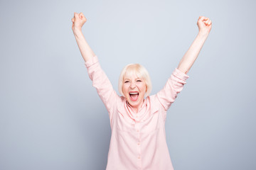 Old blonde glad excited lady smiling, laughing, raising hands up, opened mouth, over grey...