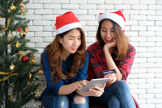 Two young cute asia women holding tablet and credit card while shopping online with happiness, Christmas holiday shopping concept