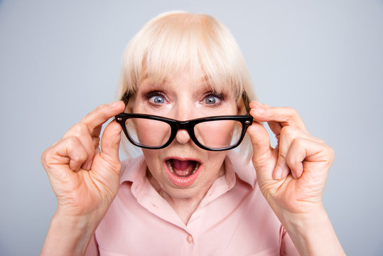 Portrait of old adult blonde caucasian lady shocked scared surprised wearing putting down eye glasses, over grey background, isolated