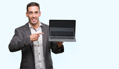 Handsome young man using computer laptop very happy pointing with hand and finger