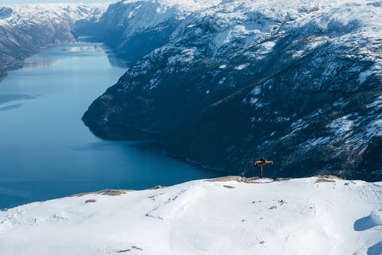 Scenic aerial view of a traveler doing funny bird pose while standing on the Pulpit Rock, Preikestolen. Beautiful winter landscape. Man hiking on the Norwegian mountains. Lysefjord, Norway