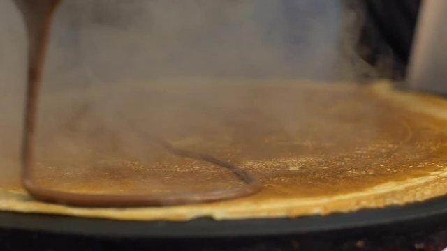 Slow motion vendor man cooking crepes on a metal griddle in Paris street. Close-up of pancake with chocolate dessert. Delicious fast food. A hand is making crepe outdoors. Cheff cook a tasty crepe-Dan
