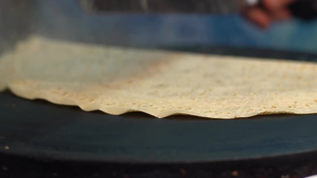 Slow motion vendor man cooking crepes on a metal griddle in Paris street. Close-up of pancake with chocolate dessert. Delicious fast food. A hand is making crepe outdoors. Cheff cook a tasty crepe-Dan