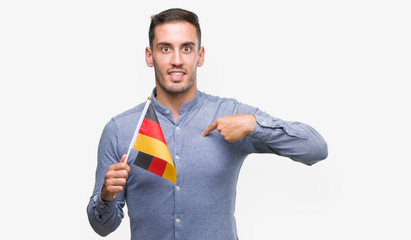 Handsome young man holding a flag of Germany with surprise face pointing finger to himself
