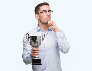 Handsome young man holding trophy serious face thinking about question, very confused idea