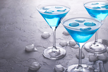 Three glasses of blue cold  martini cocktail with ice and clear dew drops on  glass on a gray concrete background , closeup shot