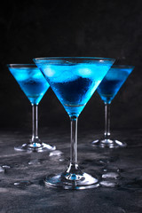 Blue cold cocktail in martini glass with ice and clear dew drops on  glass on a dark concrete background