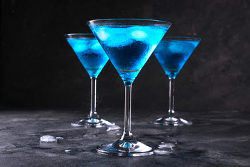 Blue cold cocktail in martini glass with ice and clear dew drops on  glass on a dark concrete background - Powered by Adobe