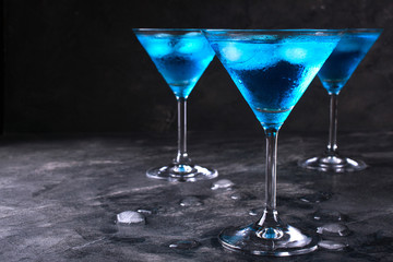 Blue cold cocktail in martini glass with ice and clear dew drops on  glass on a dark concrete background