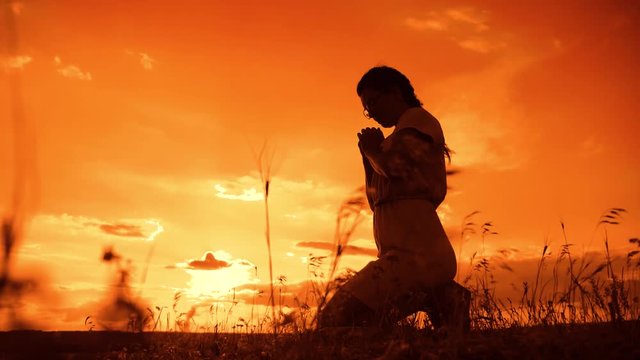 the girl prays. Girl folded her hands in prayer silhouette at sunset. slow motion video. Girl folded her hands in prayer pray to God. girl praying asks forgiveness for sins of repentance. believing
